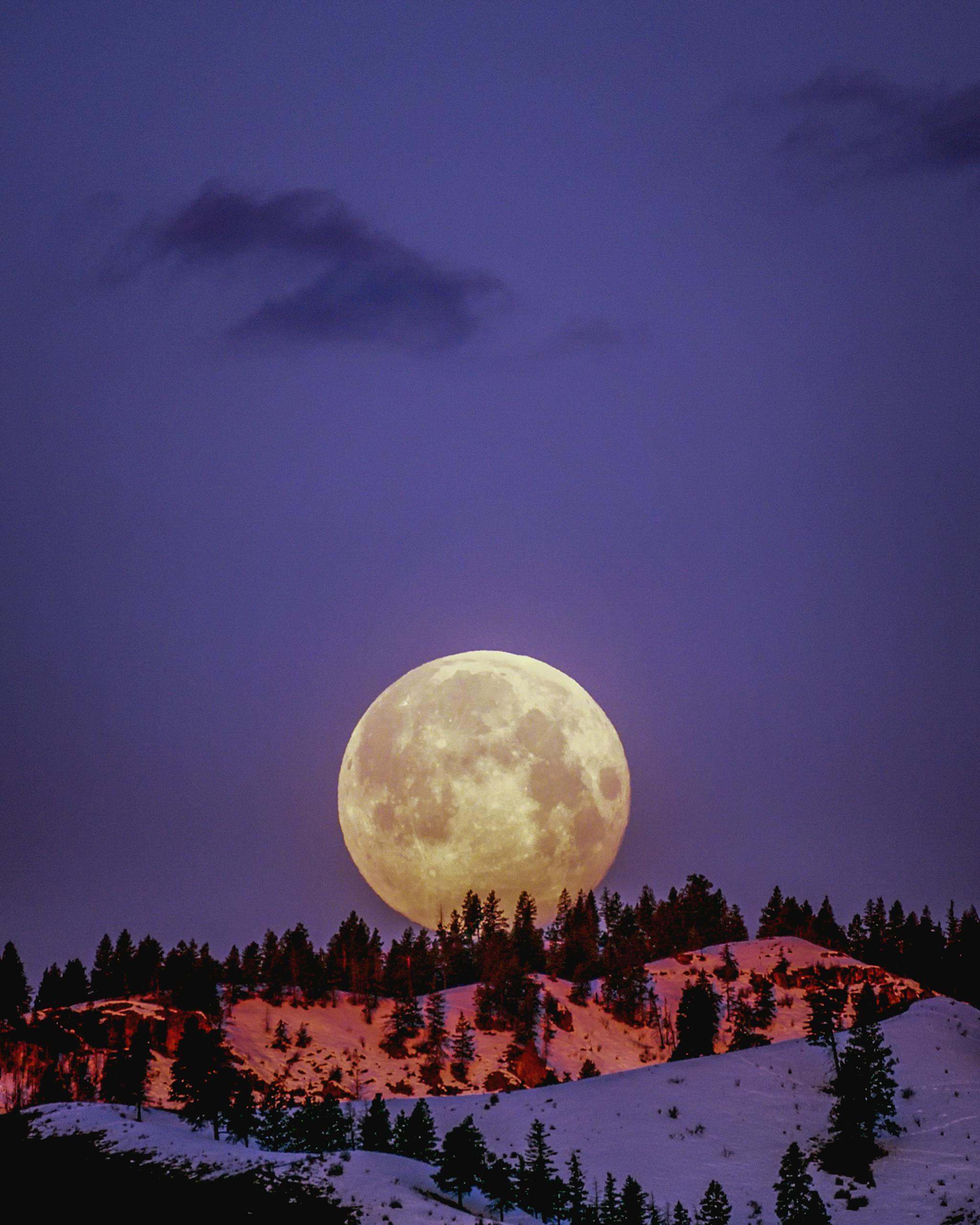 A breathtaking supermoon illuminating snow-covered hills under a purple sky in Wenatchee, WA.