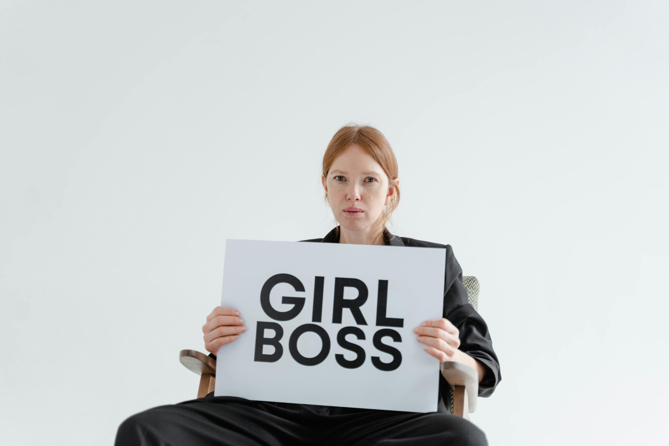Confident woman in a suit holding a GIRL BOSS sign, embodying leadership and empowerment.
