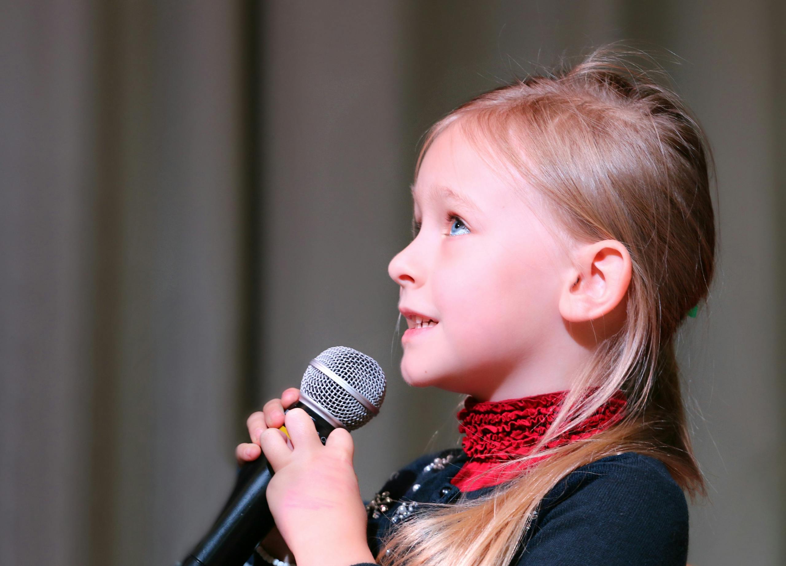 Cute young girl passionately speaking into a microphone on stage, captured in a close-up profile view.